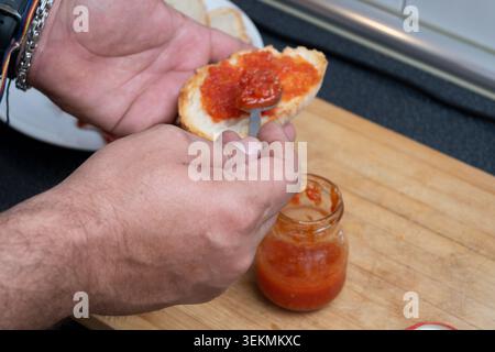 Frische Tomaten mit einem Löffel von Hand auf Baguetteschneide verteilen Stockfoto