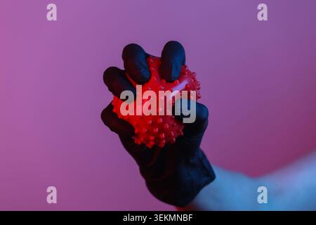Pandemiethema covid-19. Hand in Schutzhandschuhen hält ein Virusstamm-Modell. Neonlicht mit rotem blauem Farbverlauf Stockfoto