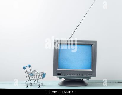 TV-Shop. Antenne altmodischer Retro-fernseher mit Mini-Supermarkt-Trolley auf weißem Hintergrund Stockfoto
