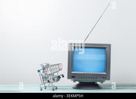 TV-Shop. Antenne altmodischer Retro-fernseher mit Mini-Supermarkt-Trolley auf weißem Hintergrund Stockfoto