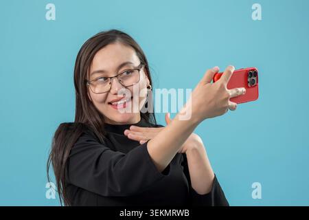 Lächelnde junge Frau, die ein Smartphone hält und Selfie im Studio macht Stockfoto