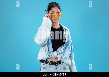 Lächelnde junge Dame, die die Sonnenbrille berührt und direkt auf das Kameraobjektiv blickt Stockfoto
