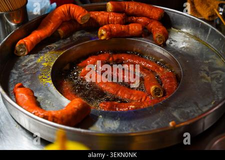 Traditionelle frittierte Schweinedärme, die in einer kochenden Ölpfanne am Temple Street Night Market unter Abendlichtern in Hongkong kochen Stockfoto