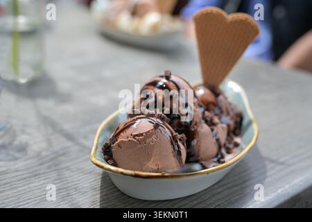Eisbecher mit Schokoladeneis, Schokoladensoße und Waffelkegel auf einem Tisch in einem Straßencafé, süßes Sommerdessert, Kopierraum, ausgewählter Fokus, Nar Stockfoto
