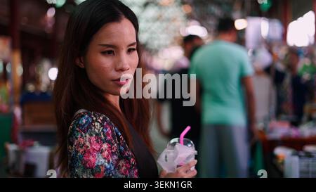 Asiatische Frau, die einen Drink-Becher in der hektischen Menge hält Stockfoto