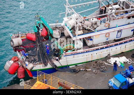 Yilan, Taiwan - 31. März 2025: Fischer bedienen ein Schleppnetz auf einem Schiffsdeck im Hafen von Nanfangao, mit Bojenflotten und einer Netzrolle, die von oben sichtbar ist. Stockfoto