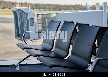 Leere schwarze Sitze im Wartebereich des Flughafens mit Außenfenster der Passagierbrücke. Stockfoto