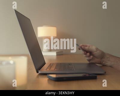 Hand eines Mannes, der die Kreditkarte in der Nähe des Laptops auf dem Tisch hält Stockfoto