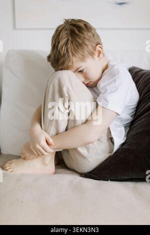 Seitenansicht eines traurigen Jungen, der sich zu Hause auf dem Sofa umarmte Stockfoto
