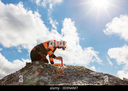 Tiefwinkelansicht des Bauarbeiters, der an sonnigem Tag auf Felsen gegen bewölktem Himmel steht Stockfoto