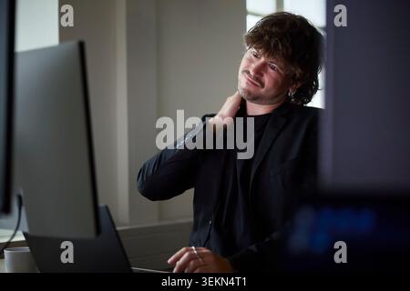 Männlicher Geschäftsmann dehnt sich während der Arbeit am Desktop-PC im Büro aus Stockfoto