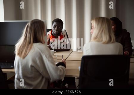 Männlicher Unternehmer, der weiblichen Kollegen zuhört, während er am Schreibtisch sitzt Stockfoto
