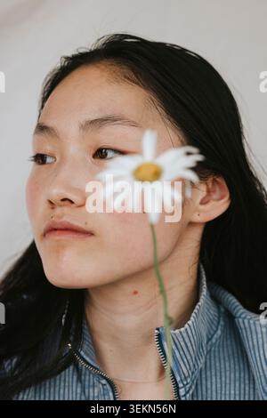 Verschwommene Gänseblümchenblume mit besinnlicher junger Frau im Hintergrund Stockfoto