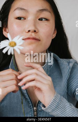 Eine nachdenkliche junge Frau, die wegschaut, während sie Gänseblümchen in der Hand hält Stockfoto