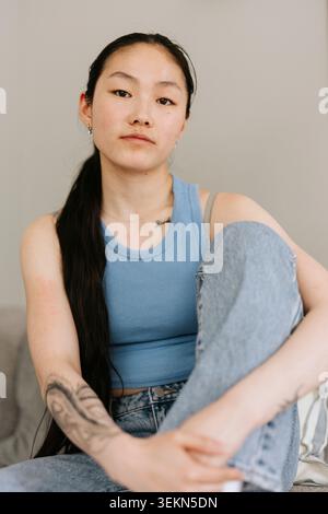 Porträt einer langhaarigen jungen Frau, die zu Hause sitzt Stockfoto
