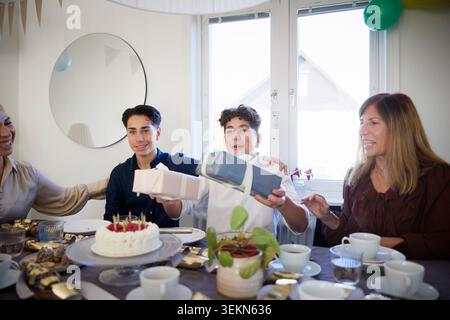 Junge erhält Geschenke von Familienmitgliedern während der Geburtstagsfeier zu Hause Stockfoto