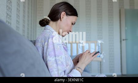 Junge Mutter mit Smartphone im Kinderzimmer Stockfoto