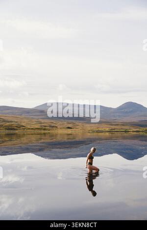 Seitenansicht einer Frau, die Freizeit im See gegen Wald schwimmt Stockfoto
