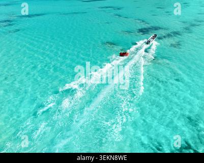Aus der Vogelperspektive eines Schnellbootes, das ein rotes Schlauchboot im transparenten türkisfarbenen Karibischen Meer in Punta Cana, Dominikanische Republik, zieht Stockfoto