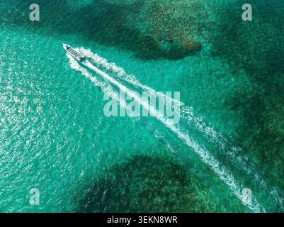 Von oben nach unten auf ein Motorboot, das durch kristallklares türkisfarbenes Meereswasser über ein Korallenriff in Punta Cana fährt Stockfoto