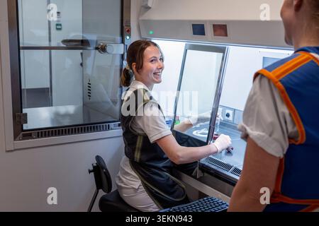 Lächelnder Wissenschaftler, der mit einem Kollegen spricht, während er in der Nähe eines Laminarkabinetts sitzt und arbeitet Stockfoto