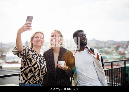 Glückliche Unternehmerin, die Selfie mit Kollegen auf dem Balkon macht Stockfoto