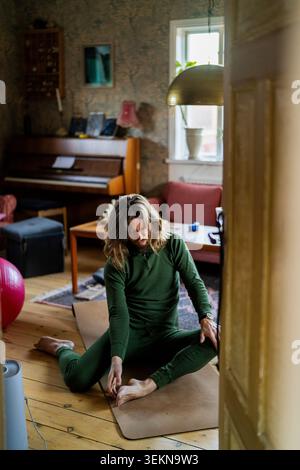 Die volle Länge des fokussierten Mannes, der die Beine dehnt, während er zu Hause auf einer Yogamatte sitzt Stockfoto