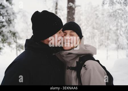 Romantischer Mann, der eine Frau küsst, die Winterjacke im Wald trägt Stockfoto