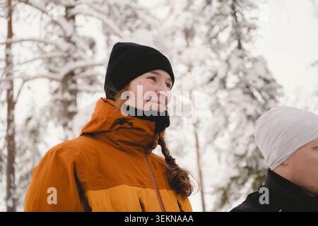 Tiefwinkelansicht eines lächelnden Mädchens mit geflochtenen Haaren im Winterwald Stockfoto