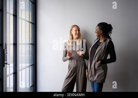 Glückliche Geschäftskollegen, die miteinander reden, während sie im Startup-Büro in der Nähe der Wand stehen Stockfoto