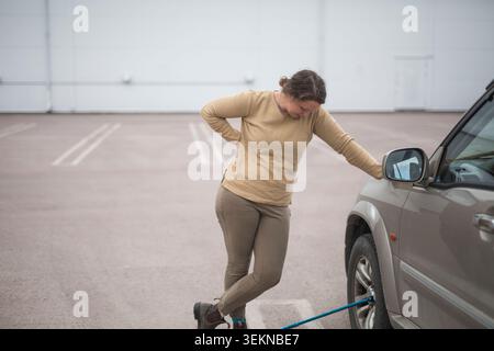 Frau, die mit der Hand auf der Hüfte steht, während sie auf den Reifenpannen des Autos blickt Stockfoto