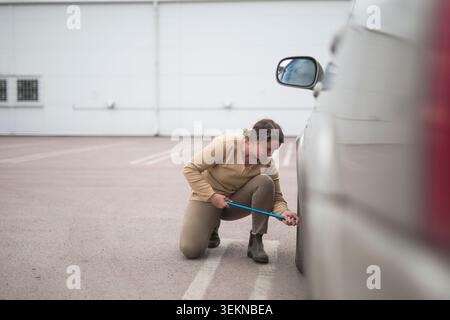 Frau hockt beim Reifenwechsel mit Radschraubenschlüssel auf dem Parkplatz Stockfoto
