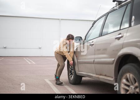 Die volle Länge einer Frau, die den Radschlüssel beim Reifenwechsel auf dem Parkplatz zieht Stockfoto