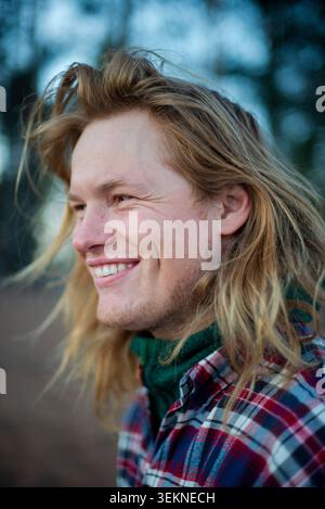 Lächelnder Mann mit langen blonden Haaren, der draußen wegschaut Stockfoto