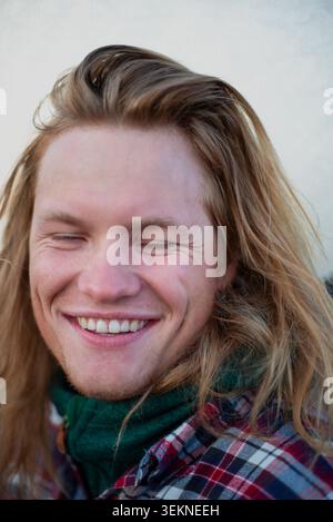 Mann mit langen blonden Haaren, der draußen lächelt Stockfoto