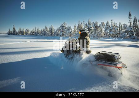 Aufnahme eines Fahrers, der mit dem Schneemobil durch den Winterwald fährt Stockfoto