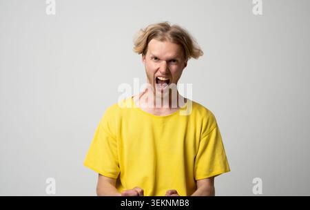 Ein junger Mann, der mit aggressivem Gesicht und offenem Mund extreme Wut und Frustration ausdrückt, symbolisiert starke negative Emotionen, Stress, Wut Stockfoto