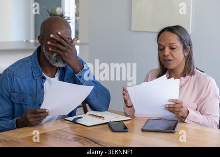 Diverse Seniorenpaare, die Papiere am Küchentisch zu Hause mit Notebook, Smartphone, Tablet bewerten. Partner, Dokumente, Haushalt, Essen, offen, Finanzen, Innenraum Stockfoto