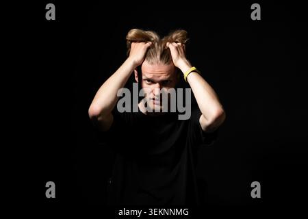 Junger Mann, der sein Haar in einem Studio-Porträt umklammert, roher Ausdruck von Frustration, Stress und Angst, die überwältigend, Burnout und emotional vermitteln Stockfoto