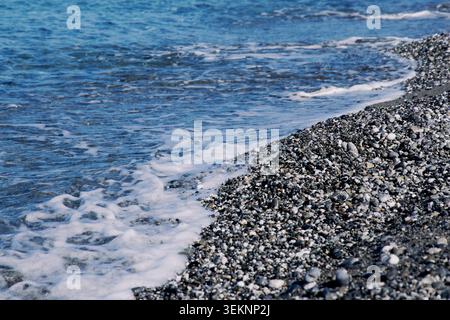 Meereswellen mit weißem Schaum über einem grauen Kiesstrand. Stockfoto