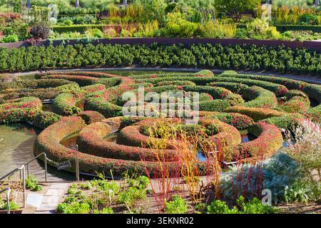 Üppig grüne und rote Heckenlabyrinth wirbelt elegant in einem kreisrunden Wasserpool im Central Garden des Getty Centers, umgeben von Terrassen-Landschaftsgärten i Stockfoto