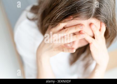 Nahaufnahme einer Frau, die starke Angst zeigt und sich Sorgen um ihr graues Haar macht. Ein reifer Erwachsener zeigt tiefe emotionale Schmerzen, wenn Silberstränge erscheinen. Mutter kann kein sichtbares Zeichen des Alterns akzeptieren. Stockfoto