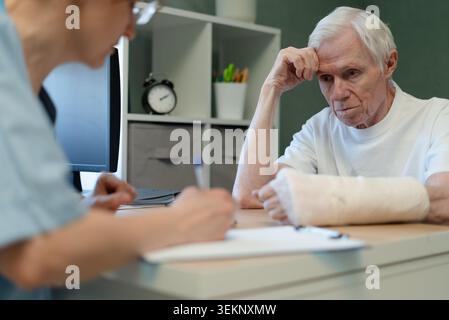 Älterer Mann bei ärztlicher Sprechstunde mit aufmerksamer Pflegefachkraft in der Klinik. Der ältere Patient hat eine gründliche Untersuchung, während das medizinische Fachpersonal Notizen macht. Älterer Mann und Frau im professionellen Büro Stockfoto