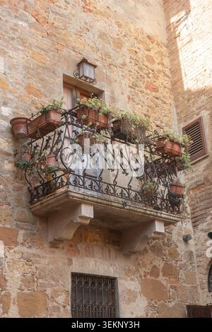 Traditionelle Steinhausfassade mit schmiedeeisernem Balkon und blühenden Blumen. Warmes mediterranes Licht unterstreicht rustikale Texturen und zeitlos Stockfoto