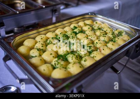 Eine Scheuerschale aus Metall, gefüllt mit traditionellen Klößen, bestreut mit frischen grünen Kräutern am Catering-Buffet. Stockfoto