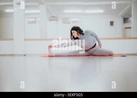 Tänzerin dehnt sich in einem Studio und macht einen Frontabschnitt auf einer Matte, der Flexibilität und Konzentration zeigt Stockfoto