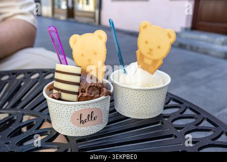Eine Nahaufnahme von zwei Pappbechern gefüllt mit Schokolade und Vanilleeis, dekoriert mit Waffelrollen und bärenförmigen Keksen, die auf einem Schwarz sitzen Stockfoto