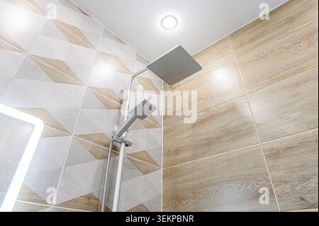 Moderne Badezimmerecke mit dualem Duschkopf und stilvollen Fliesenwänden in geometrischer Holzoptik. Sauber und gut beleuchtet, mit zeitgenössischem Design Stockfoto