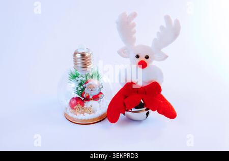 Niedlicher Weihnachtshintergrund mit einem weichen Rentierspielzeug mit roter Nase und festlicher Glocke neben einem dekorativen Weihnachtsmann-Ornament Stockfoto