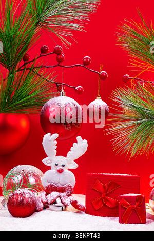 Rote Weihnachts-Geschenkboxen mit Schleife, Rentierplüsch und farbenfrohen Kugeln auf weichem, schneebedeckten Hintergrund mit festlicher Einrichtung. Stockfoto